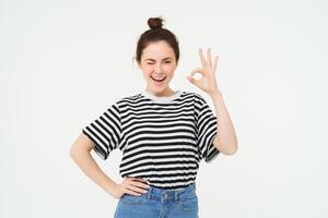 excelente elección. sonriente elegante joven mujer, demostración bueno, Okay gesto, cero firmar, en pie terminado blanco antecedentes foto