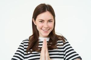 Portrait of woman showing namaste gesture, holding palms clenched together near chest, standing isolated over white background photo