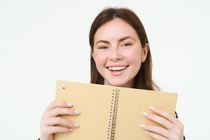 Portrait of happy woman smiling, showing her book, daily planner, holding notebook, planning her trip an writing notes in organizer, isolated against white background photo