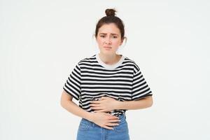 Woman feeling hungry, touching her belly. Girl with period cramps, menstrial pain, holds hands on stomach that aches, isolated over white background photo