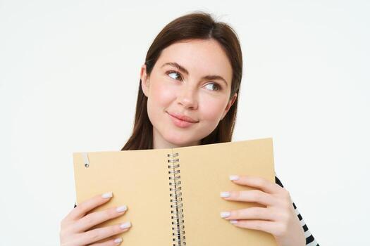 retrato de hermosa joven mujer, participación diario planificador, escritura en su diario, haciendo notas en cuaderno y sonriente, soñando acerca de algo, en pie pensativo en contra blanco antecedentes foto