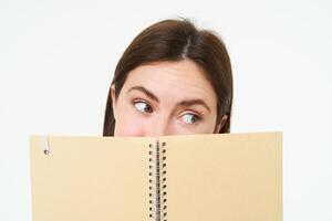 Image of woman reading something interesting in notebook, holding planner and making a side eye, standing over white background photo