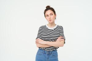 Image of intrigued young woman, thinking, pucker lips with thoughtful face, cross arms on chest, standing over white background photo