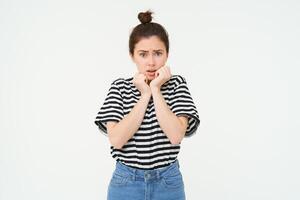 Portrait of scared, timid young woman, gasping, shaking from fear, looks frightened, stands over white background photo