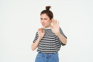 Disgusted woman steps back, raising hands defensive, avoiding something, rejecting and refusing offer, standing over white background photo