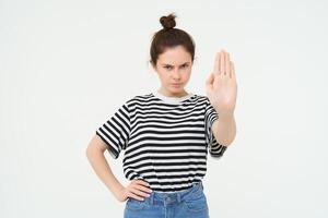 Image of woman frowning, showing one palm, stop gesture, disapprove and reject something, makes prohibit gesture, standing over white background photo