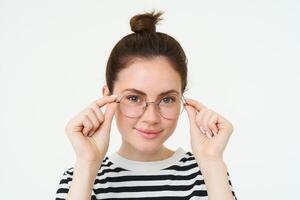 Close up portrait of smiling, attractive young woman wearing new eyewear, trying on glasses for vision, standing over white background photo