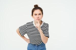 Angry woman shushing, hush at you, press finger to lips, tells to keep quiet, arguing, scolding someone, standing over white background photo