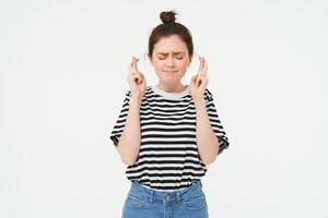 Nervous girl, student cross fingers for good luck, making wish, hoping for something, anticipating positive results, standing over white background photo