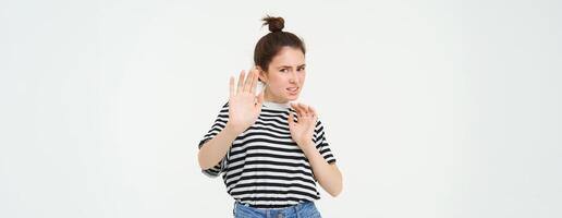 Disgusted woman steps back, raising hands defensive, avoiding something, rejecting and refusing offer, standing over white background photo