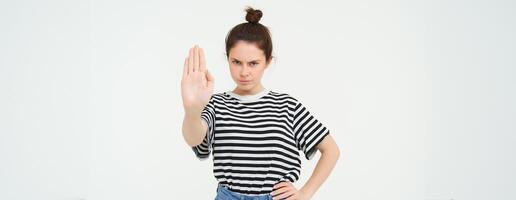 Image of woman frowning, showing one palm, stop gesture, disapprove and reject something, makes prohibit gesture, standing over white background photo