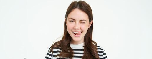 Portrait of happy, beautiful young woman, smiles and winks at you, stands over white background photo