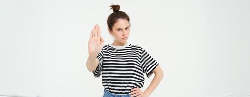 imagen de hermosa mujer con grave rostro, demostración detener firmar, extiende uno palma y frunce el ceño, soportes terminado blanco antecedentes foto