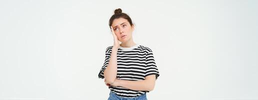 Portrait of young distressed woman sighs, looks up with sad, tired face expression, stands over white background photo