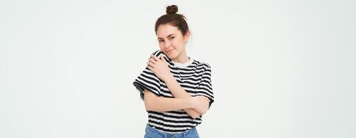 Image of tender, beautiful brunette girl, hugging herself, concept of selfcare and love, standing over white background photo