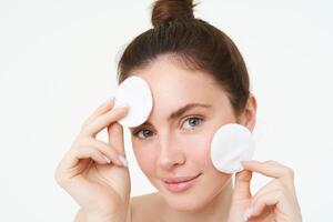 Portrait of young woman cleansing her face, takes off her makeup, washing her face, using skincare routine with cotton pads, isolated over white background photo