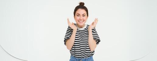 Portrait of woman reacts to amazing news, claps hands and smiles, pleased by smth, stands over white background photo