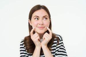 belleza y mujer concepto. joven sonriente mujer, demostración su linda hoyuelos en cara y mirando feliz, positivo emoción, hermosa cara sin imperfecciones, en pie terminado blanco antecedentes foto