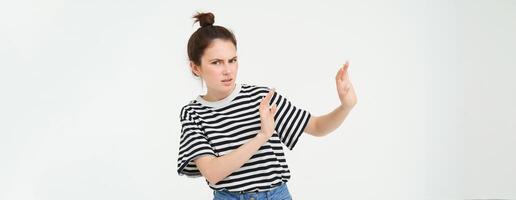 Image of woman expressing aversion, dislike something, looks apalled, extends hands forward in defensive gesture, rejecting, refusing, standing over white background photo