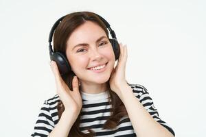 Portrait of beautiful woman in wireless headphones, listening music, using earphones, smiling at camera, standing over white background photo