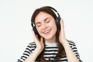 retrato de hermosa mujer en inalámbrico auriculares, escuchando música, utilizando auriculares, sonriente a cámara, en pie terminado blanco antecedentes foto