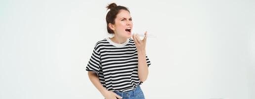 Angry woman shouts at mobile phone, argues at someone over the telephone, has intense conversation over smartphone, white background photo