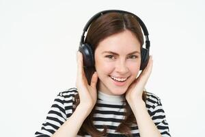 Portrait of woman, smiling, wearing wireless headphones, listening music, studying in earphones, standing isolated over white background photo