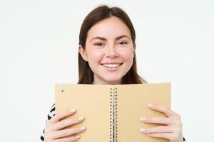 Portrait of young woman makes notes in her planner, writes in diary, checks her schedule in notebook, holding organizer in hands, stands over white background photo