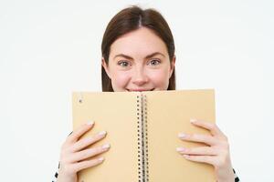 Image of young woman with notebook, holding her personal diary, work planner, smiling, reading something, standing over white background photo