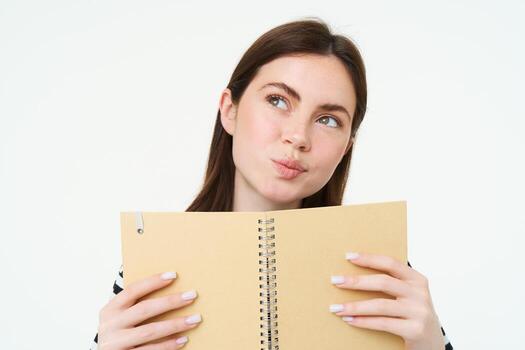 retrato de joven mujer hace notas en su planificador, escribe en diario, cheques su calendario en computadora portátil, participación organizador en manos, soportes terminado blanco antecedentes foto
