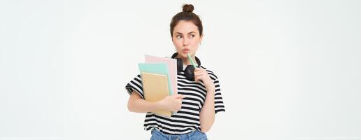 estudiante y educación concepto. joven mujer con libros, notas y bolígrafo en pie terminado blanco fondo, Universidad niña con auriculares terminado cuello posando en estudio foto