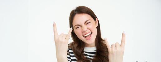Let it rock. Excited, laughing young woman, showing heavy metal, horns gesture and smiling, having fun, expressing positivity and joy, standing over white background photo