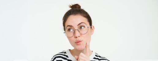 Image of woman in glasses, thinking, pondering smth, looking away with thoughtful face, analizing, standing over white background photo