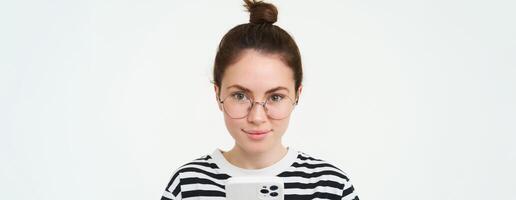 Portrait of beautiful young woman in eyewear, holding smartphone, using mobile phone, online shopping in application, standing over white background photo