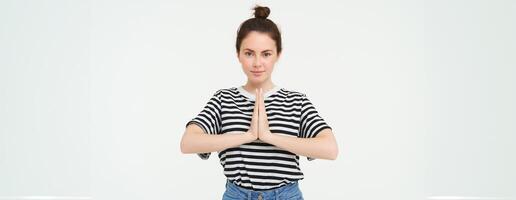 Image of young woman shows namaste gesture, holds hands together, says thank you, expresses gratitude, stands over white background photo