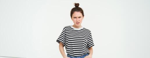 Image of bothered, disappointed young woman, frowning, complaining, looking angry and upset, standing over white background, arguing photo