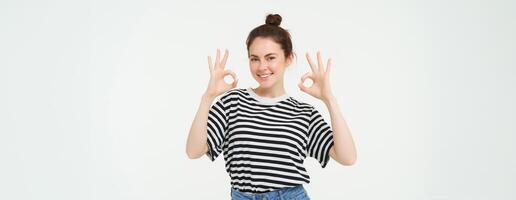 Excellent choice. Smiling stylish young woman, showing okay, ok gesture, zero sign, standing over white background photo