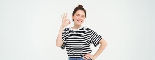No problem, excellent choice. Smiling, confident young woman, showing okay, ok sign, zero gesture, recommends product, stands over white background photo