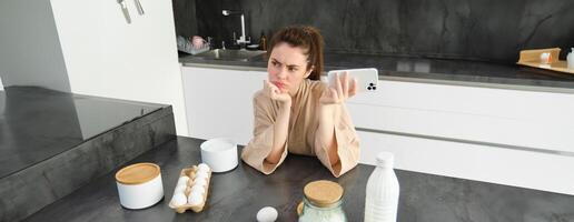 Attractive young cheerful girl baking at the kitchen, making dough, holding recipe book, having ideas photo