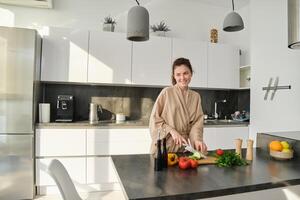 retrato de guapo mujer Cocinando ensalada en el cocina, el cortar vegetales y sonriente, preparando sano comida, líder sano estilo de vida y comiendo crudo comida foto