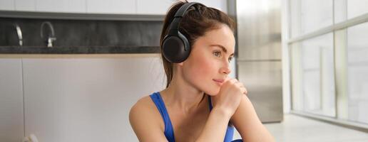 Close up portrait of beautiful brunette woman, wearing headphones, listening to music and working out, smiling and looking aside thoughtful photo