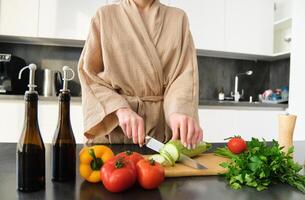 Close up portrait of female hands, woman wearing robe, cutting vegetables on chopping board, cooking vegan dinner, vegetarian meal for family, standing in kitchen photo