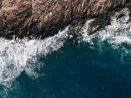 Top view Azure blue sea with waves beating on beach and rocks. Aerial photo