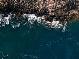 Top view Azure blue sea with waves beating on beach and rocks. Aerial photo