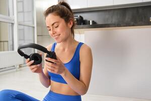 Portrait of woman in tracksuit, doing yoga training, workout at home with wireless headphones, listening music to focus photo