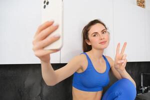 ajuste y sano joven Deportes mujer, demostración paz firmar, tomando selfie en ropa activa, aptitud blogger haciendo fotos para social medios de comunicación en su ropa deportiva