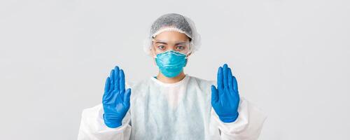 Covid-19, coronavirus disease, healthcare workers concept. Close-up of serious-looking concerned asian female doctor in personal protective equipment show stop gesture, prohibit enter dangerous zone photo