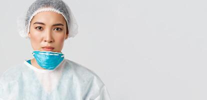 Covid-19, coronavirus disease, healthcare workers concept. Close-up of tired, exhausted asian female doctor take-off respirator and protective glasses, nurse have skin damage after shift at hospital photo