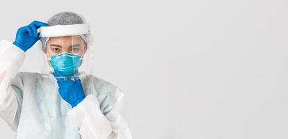 Covid-19, coronavirus disease, healthcare workers concept. Confident serious-looking female asian doctor, put on face shield and respirator, personal protective equipment, white background photo