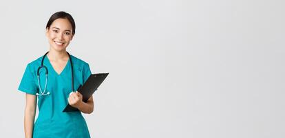 Healthcare workers, preventing virus, quarantine campaign concept. Smiling asian female nurse, doctor with clipboard wearing scrubs, provide checkup, examine patient in clinic, white background photo